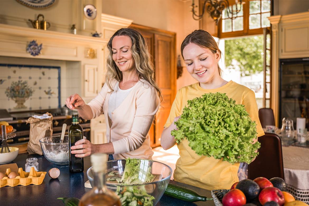 Teenage girl and mother preparing a balanced meal with fruit, vegetables, and nutritious foods to support healthy growth during puberty.
